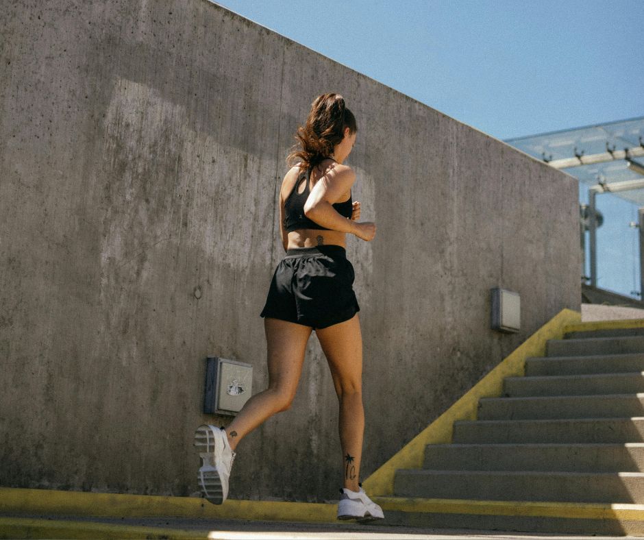 Woman dressed in black sports bra and black shortsrunning towards a staircase